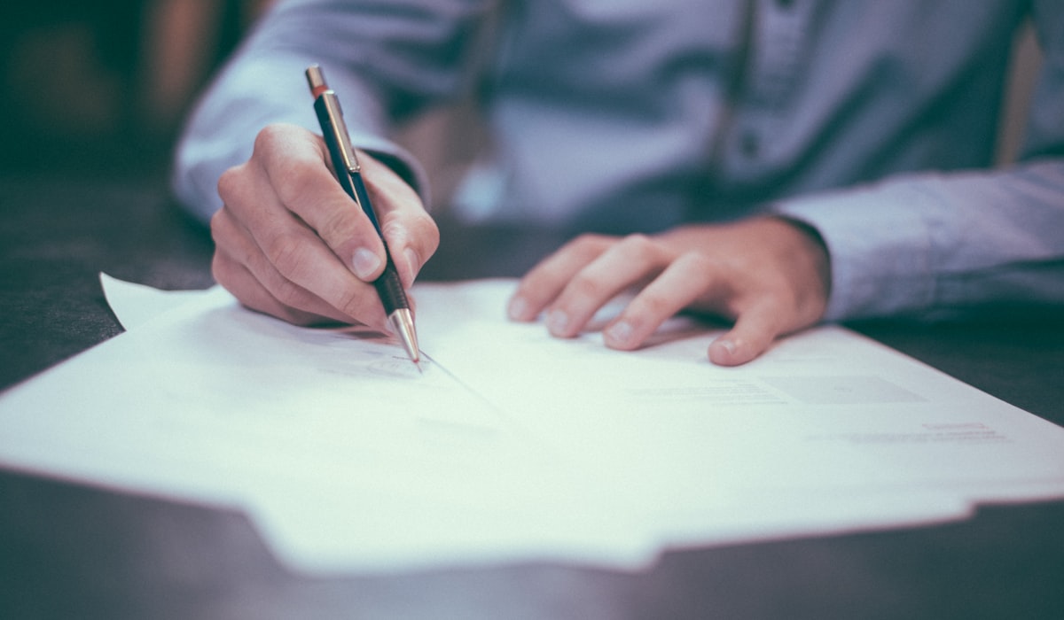 Contrato claro passa profissionalismo. Cliente costuma ficar mais tranquilo, não mais desconfiado Pessoa assinando documento: contrato claro protege os dois lados
