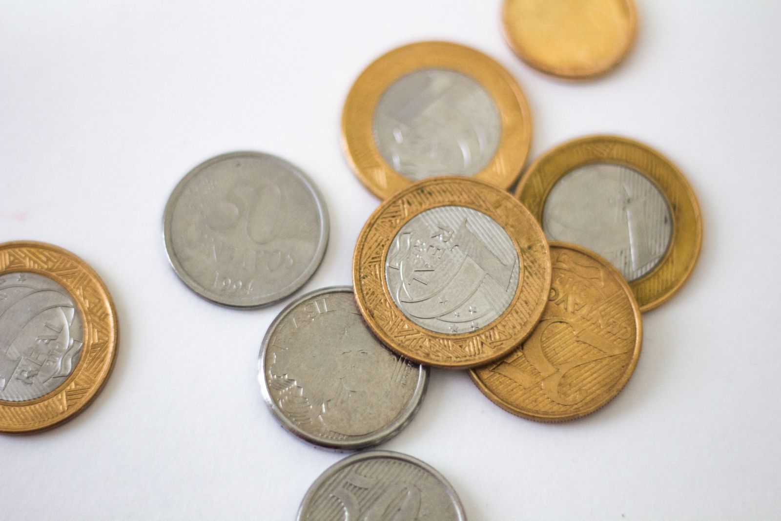 Moedas de real brasileiro espalhadas sobre uma superfície branca
