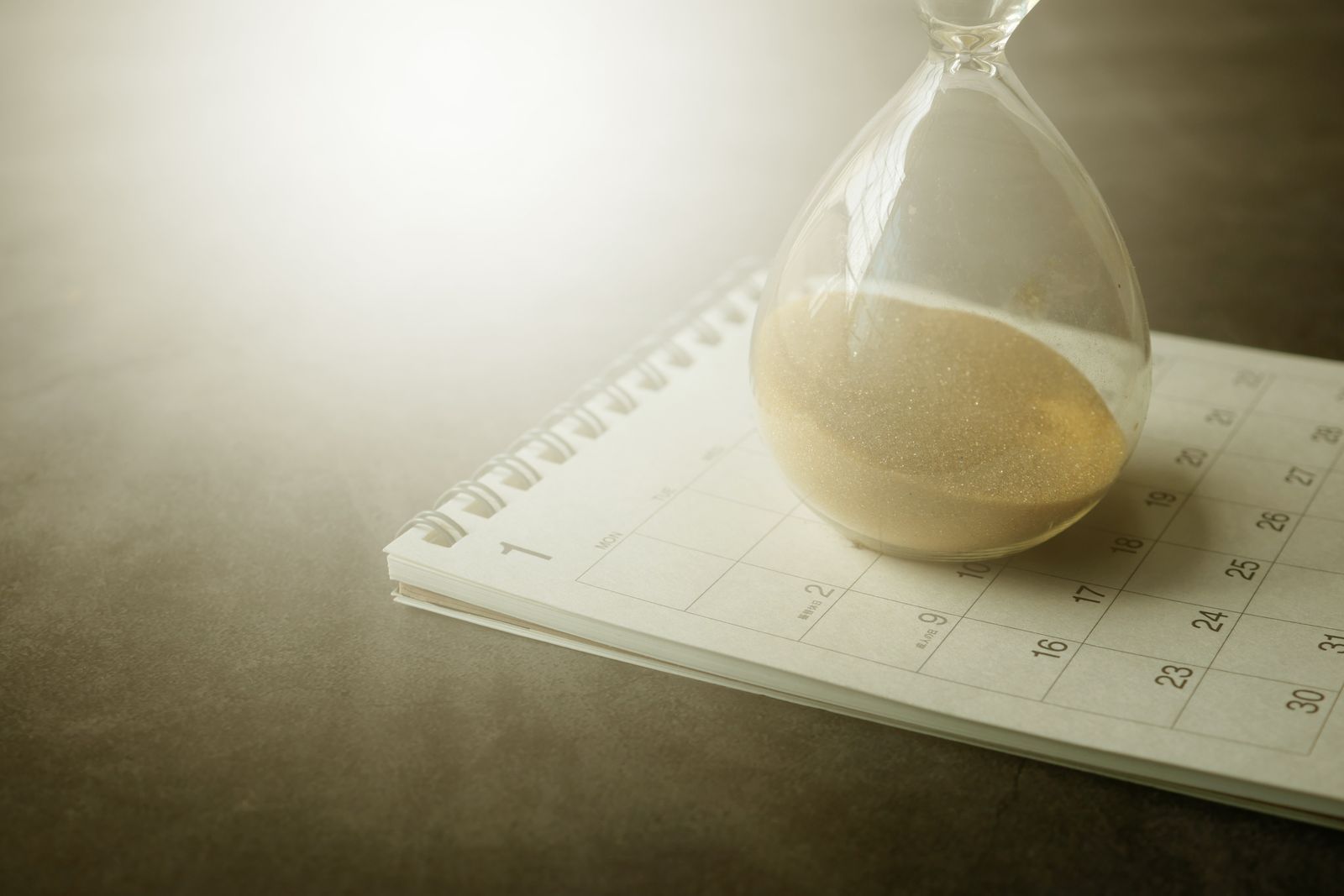 Ampulheta sobre um calendário de mesa, simbolizando o tempo correndo até o prazo de entrega